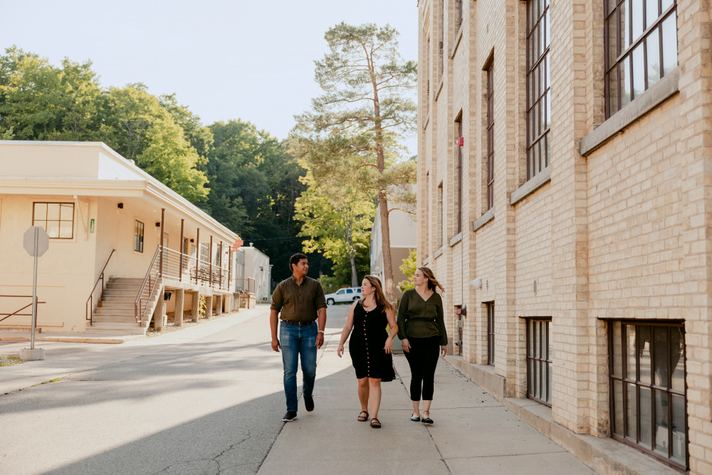 Three young professionals standing and talking to each other on a road between two light colored brick buildings