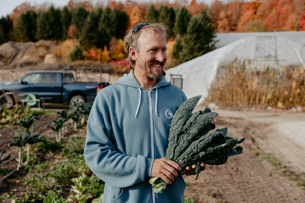 9 Beans Row owner Nic Wetly holding a piece of kale with his farm in the background