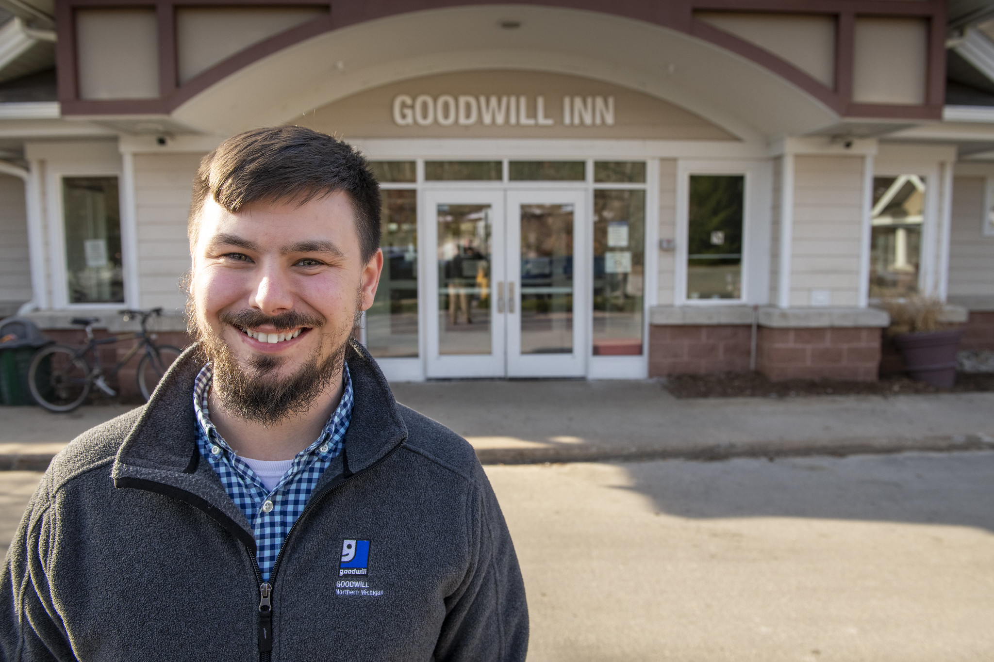 Smiling person wearing a Goodwill Northern Michigan jacket stands outside the entrance to Goodwill Inn.