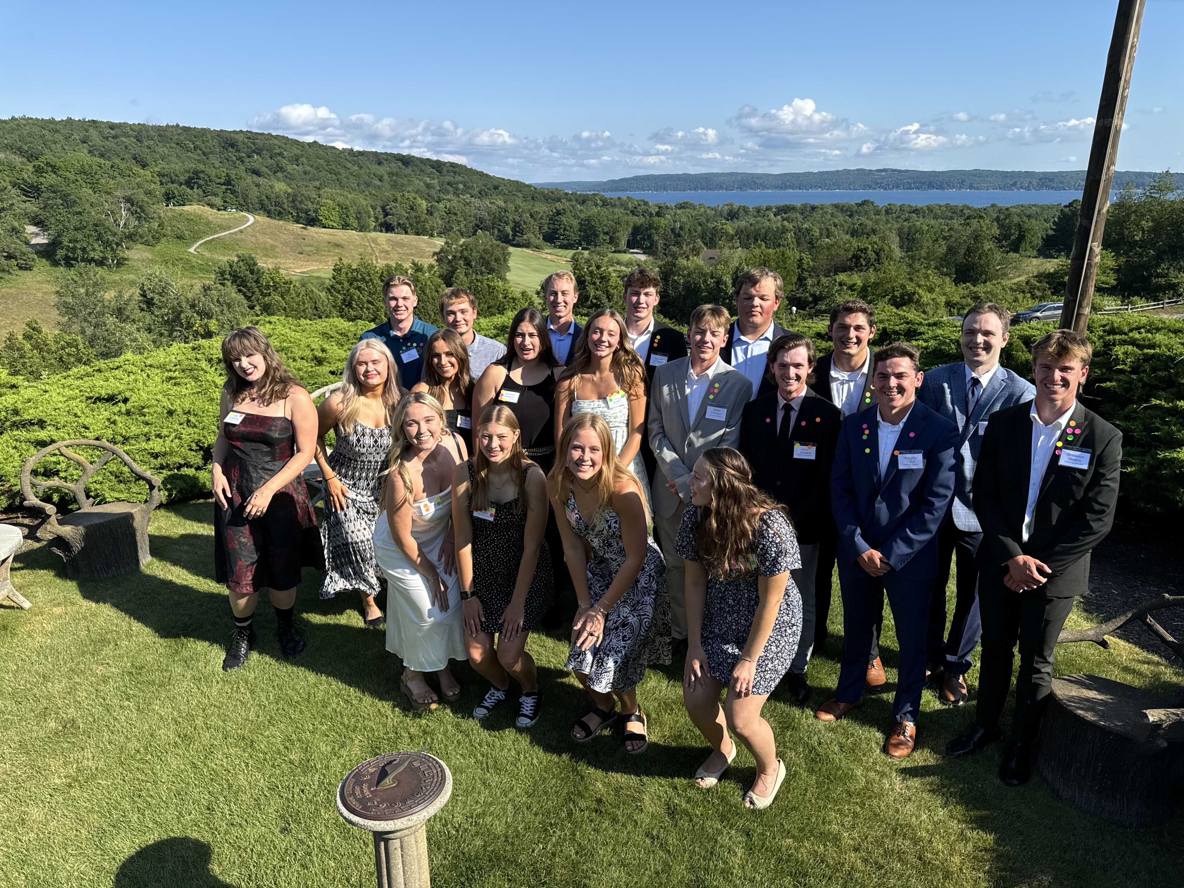  A group of 2024 Crystal Downs Country Club scholarship recipients standing together outside on a sunny day with the scenic golf course in the background.
