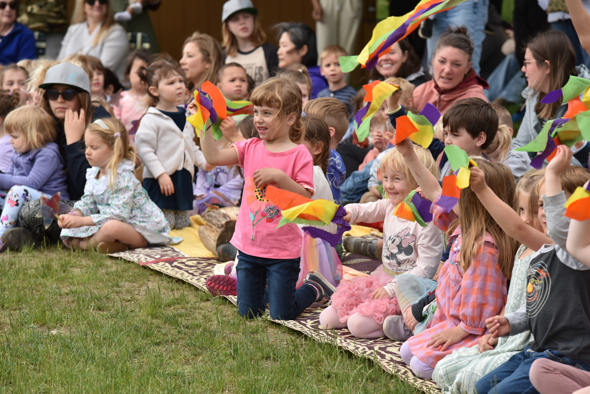Students from The Children's House sitting together on a lawn with partners holding colorful flags