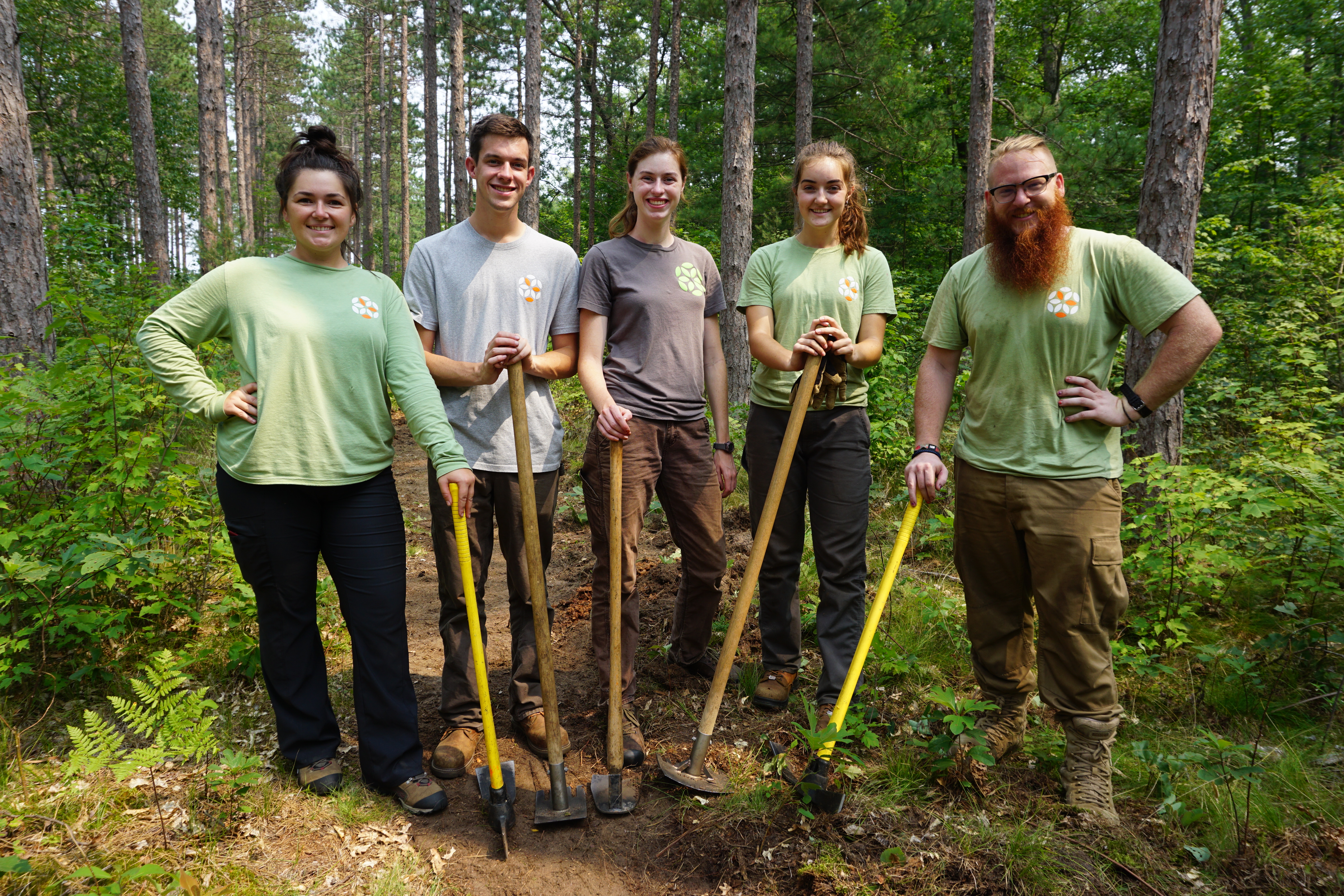 Five SEEDS EcoCorps staff holding trail‑work tools in a forest