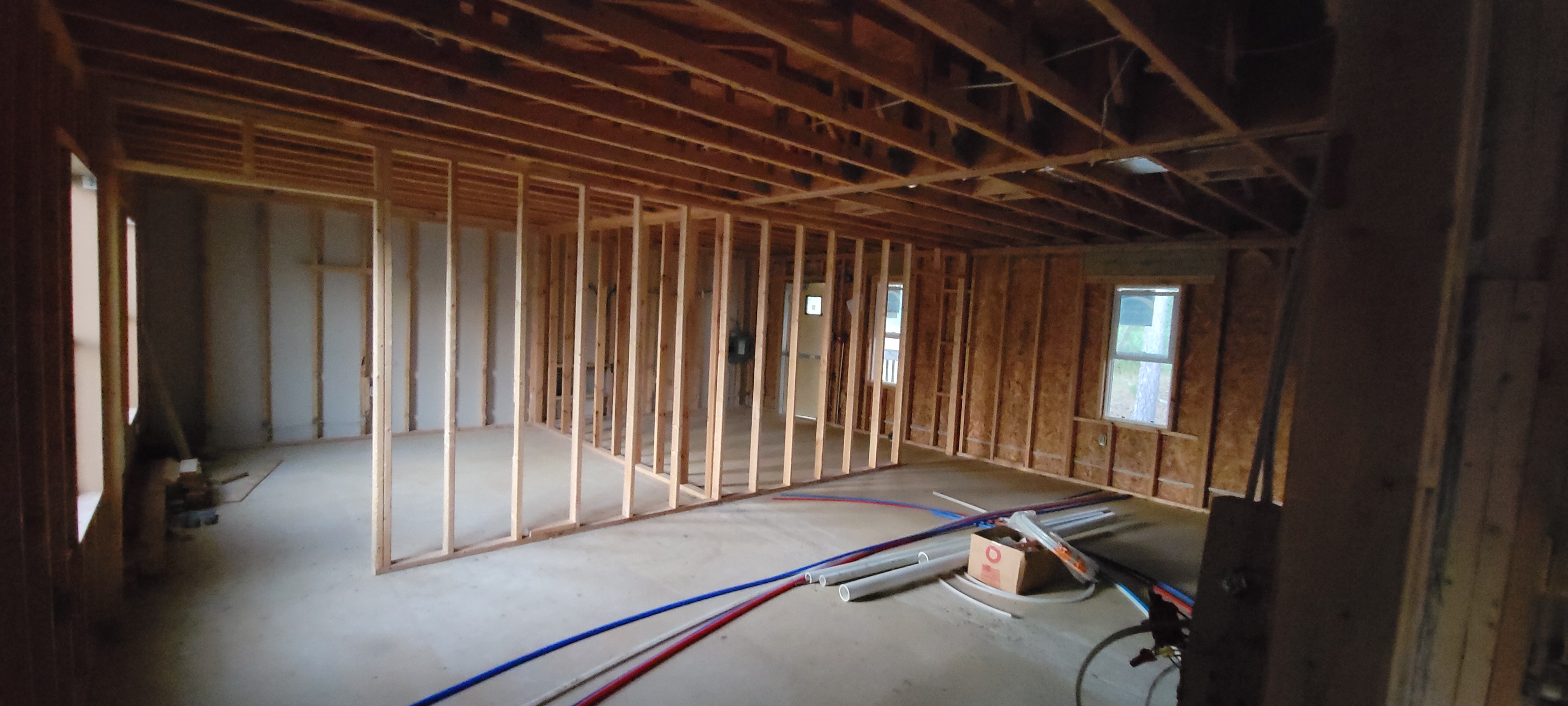 An interior view of the future apartments at 22 2 None, showing exposed wooden framing, open ceiling joists, and scattered plumbing materials on the concrete floor.