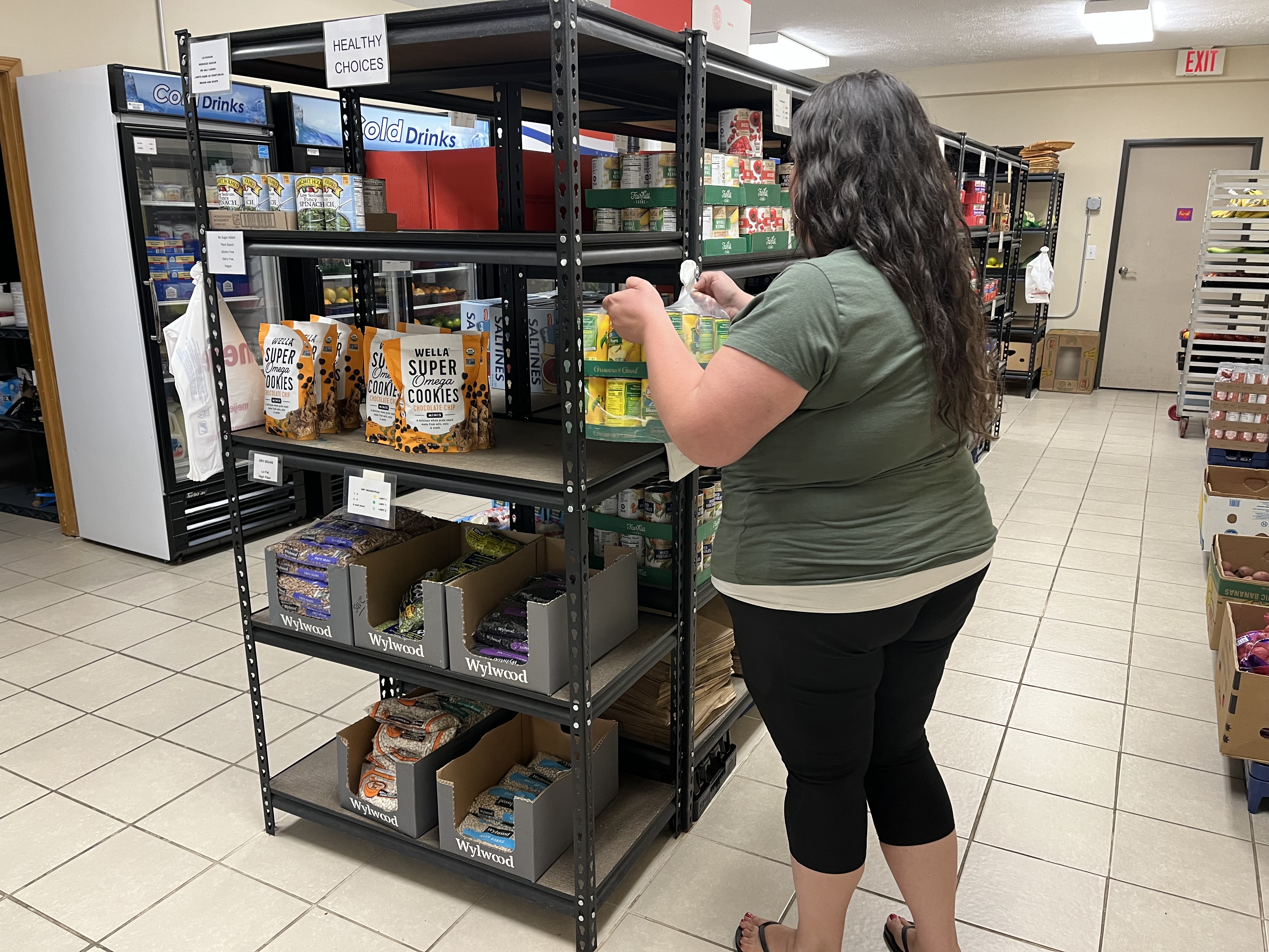 A visitor selects groceries from stocked pantry shelves at Acme Christian Thrift Store and Food Pantry, where families can access a variety of food and household essentials.