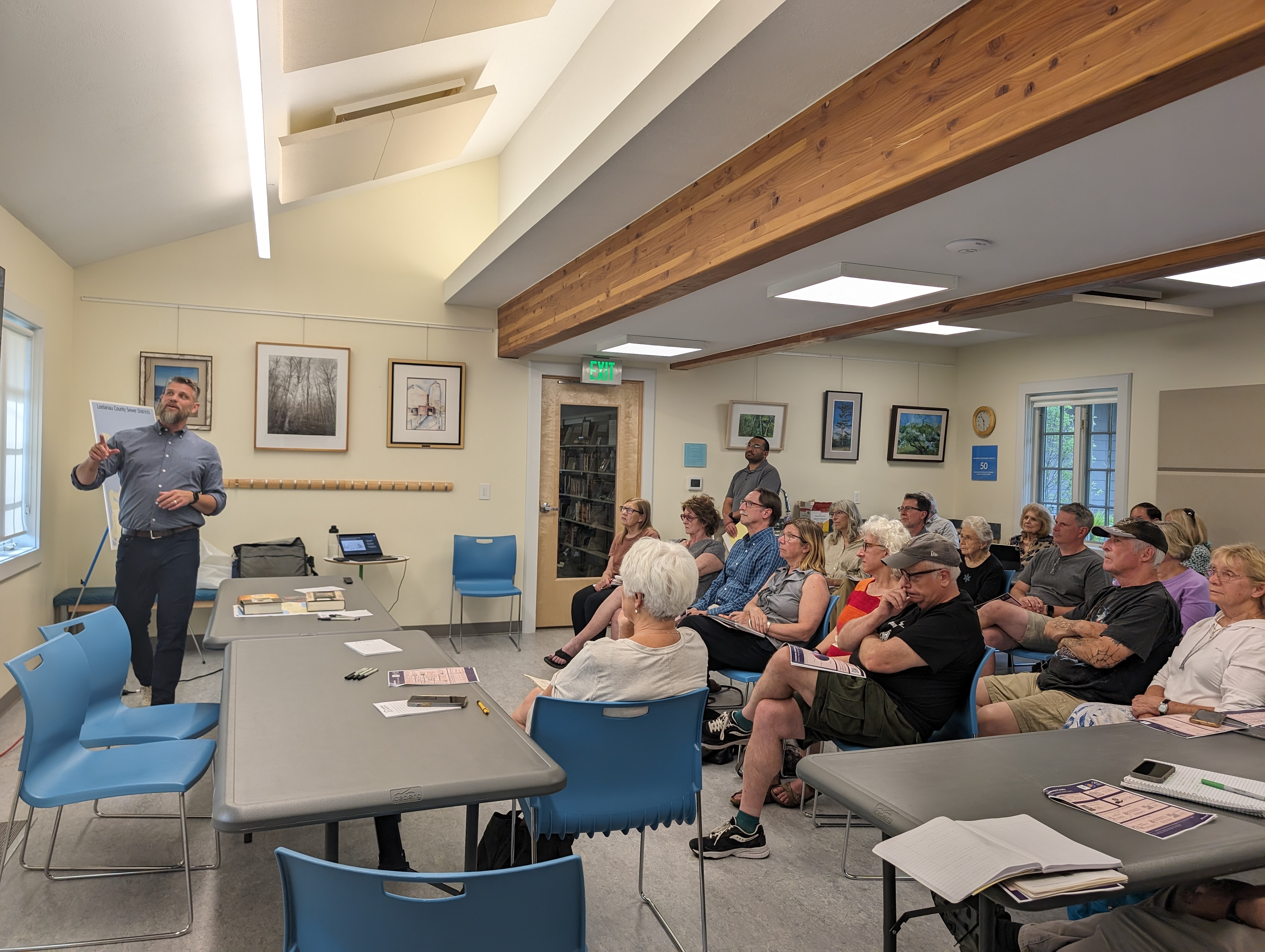 Participants seated at tables during a Housing North focus group, listening to a presenter at the front of the room. The space includes framed pictures, wooden ceiling beams, and papers and notebooks on the tables.